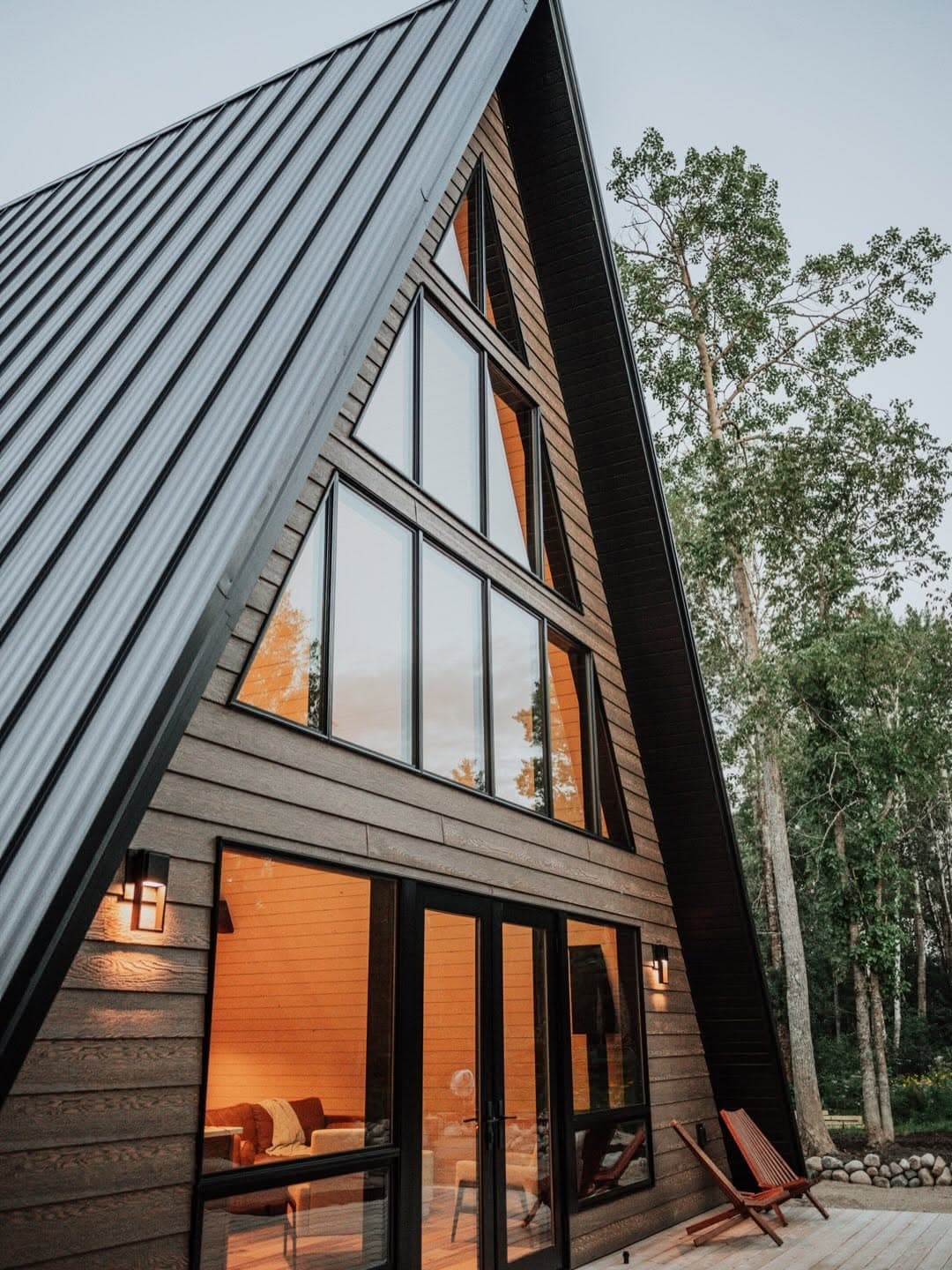 Modern A-frame cabin exterior with glowing windows among birch trees