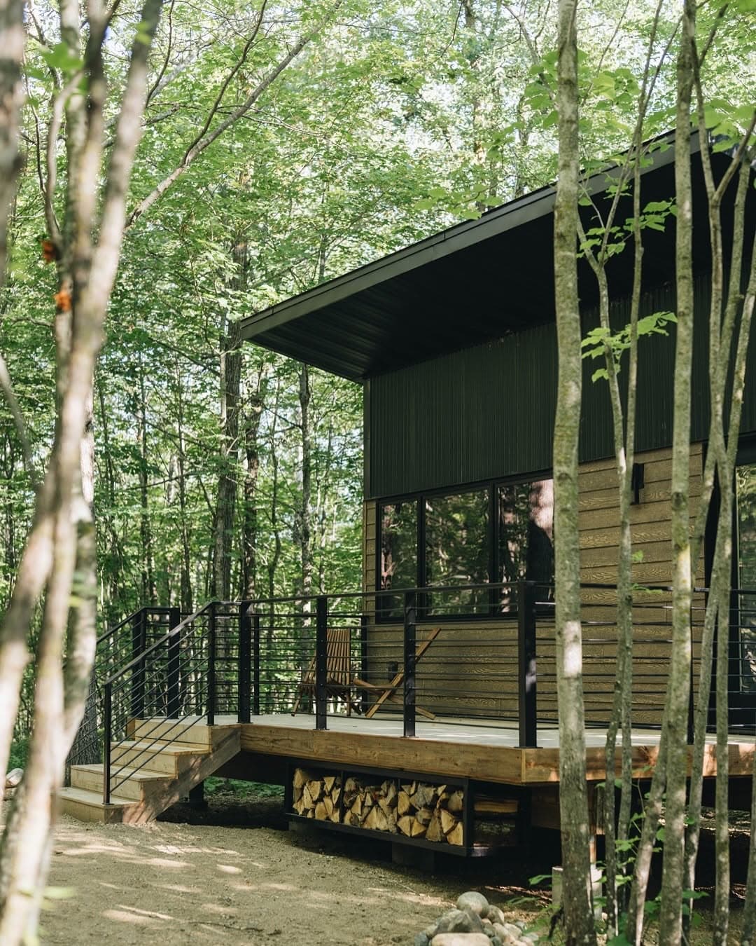 Modern tiny cabin with dark corrugated metal siding and covered porch in dense forest