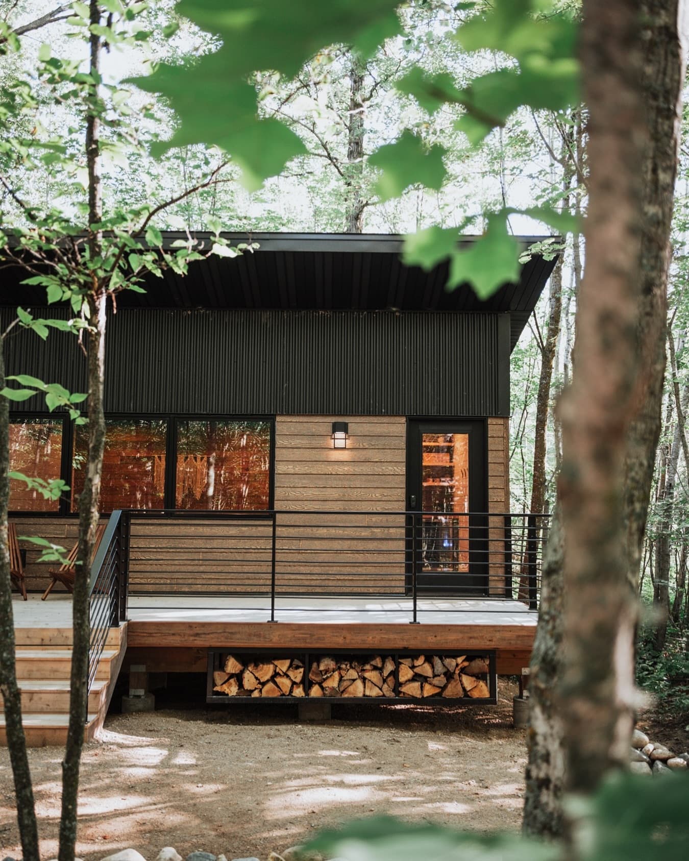 Modern rectangular tiny cabin elevated on deck, surrounded by birch and evergreen forest