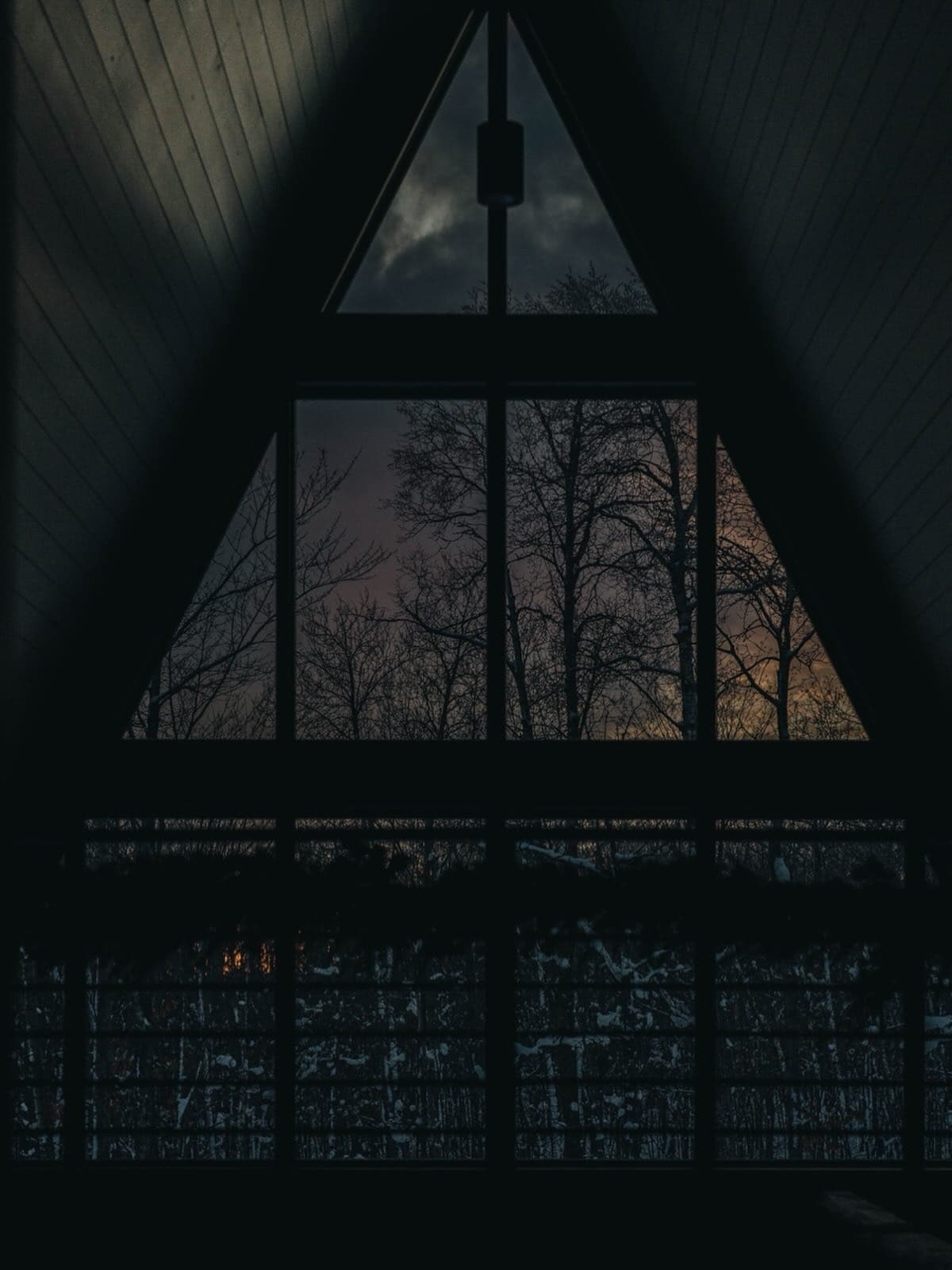 View from inside A-frame through large triangular windows at dusk
