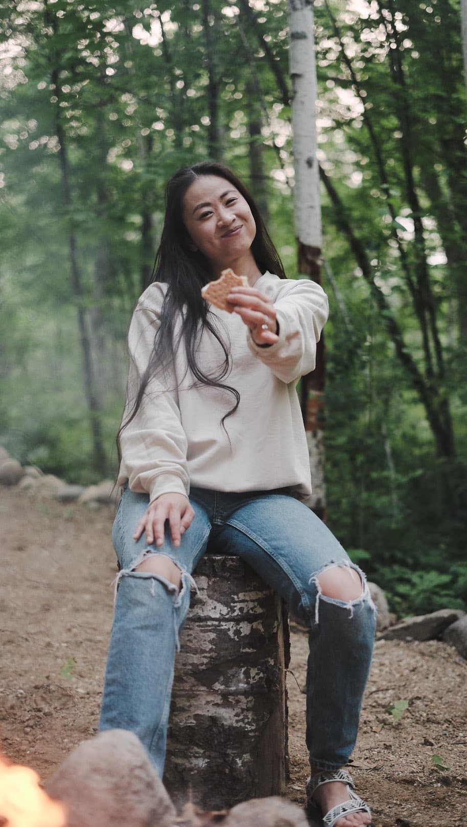 Young woman roasting marshmallow over campfire in forest