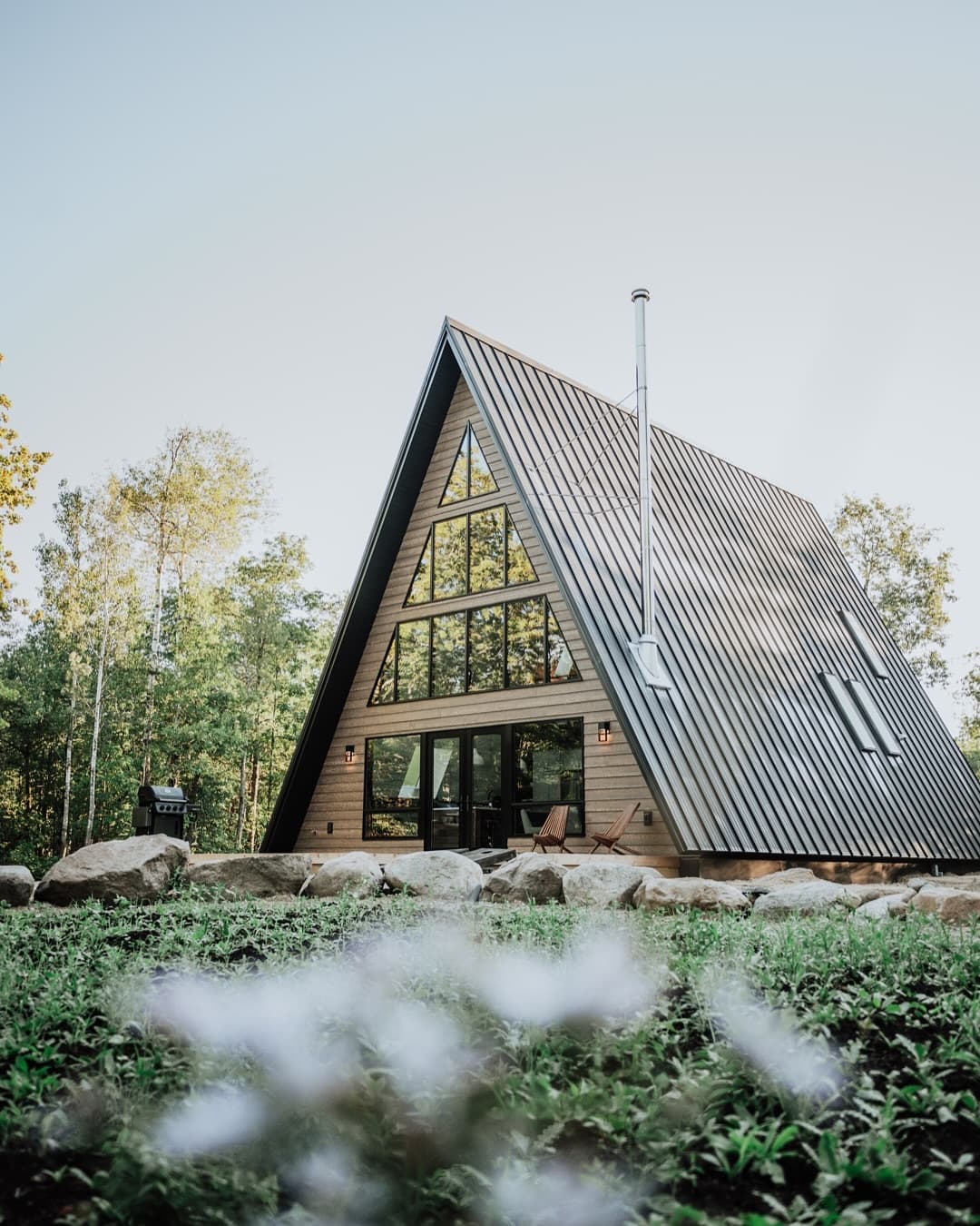 Modern A-frame cabin with corrugated metal roof and timber siding in morning light