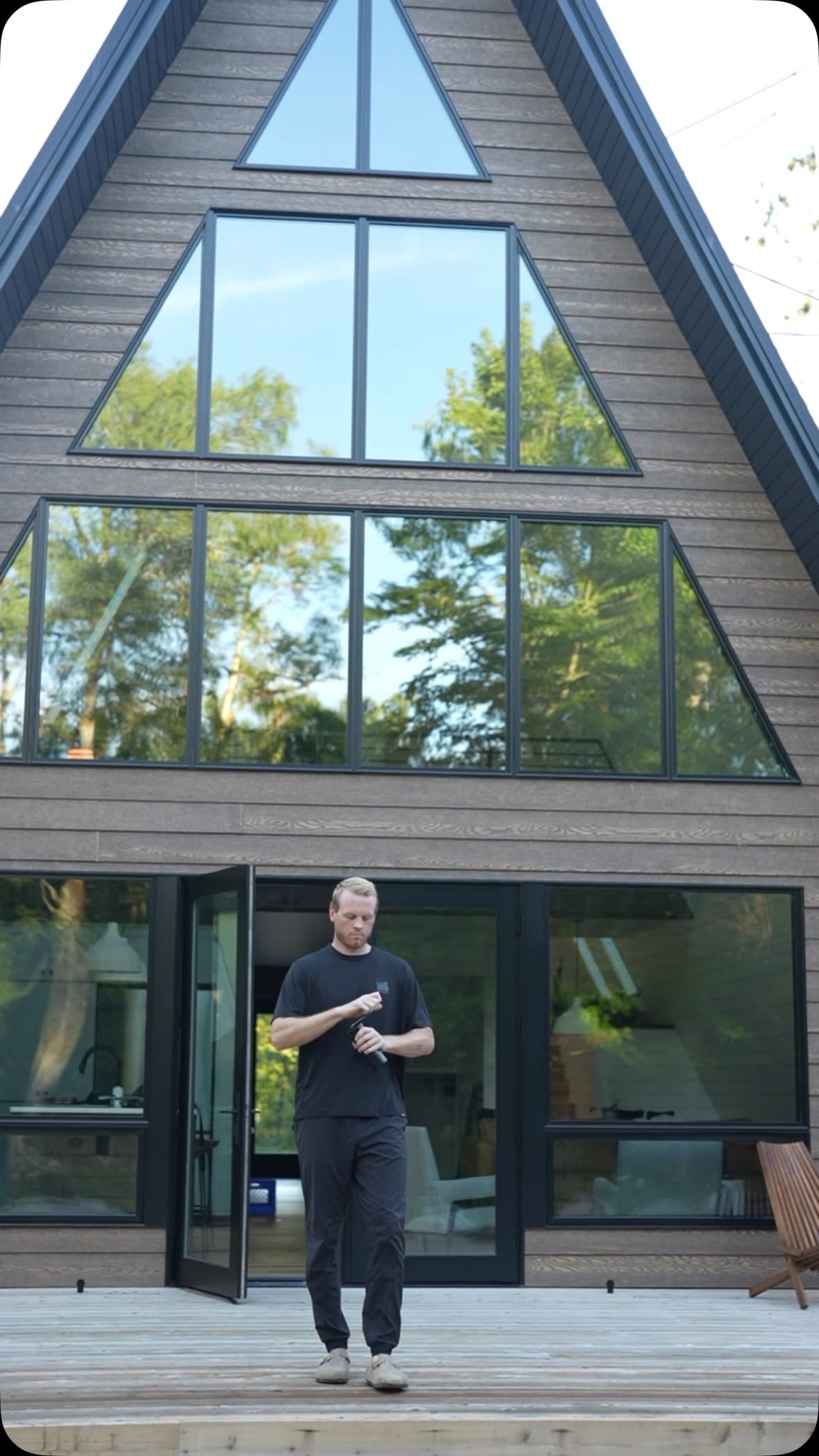 Person standing on deck in front of A-frame triangular windows holding coffee